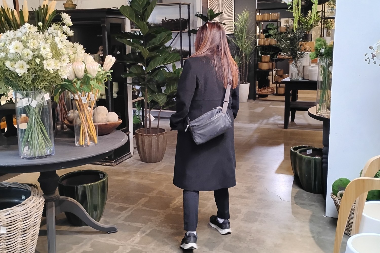 A woman walking through a bright home-and-garden shop, past vases of white flowers