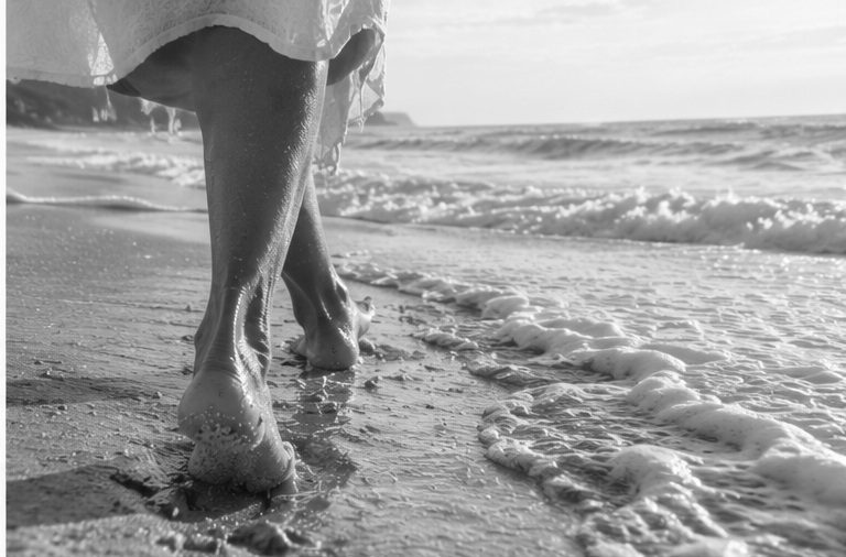 Bare feet on wet sand and sea foam, in black and white